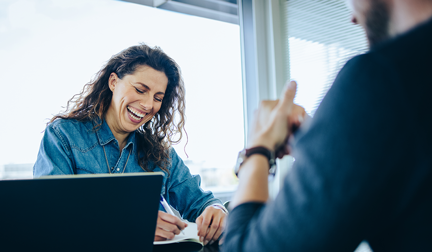 Eine dunkelhaarige Frau lacht während eines Bewerbungsgesprächs.