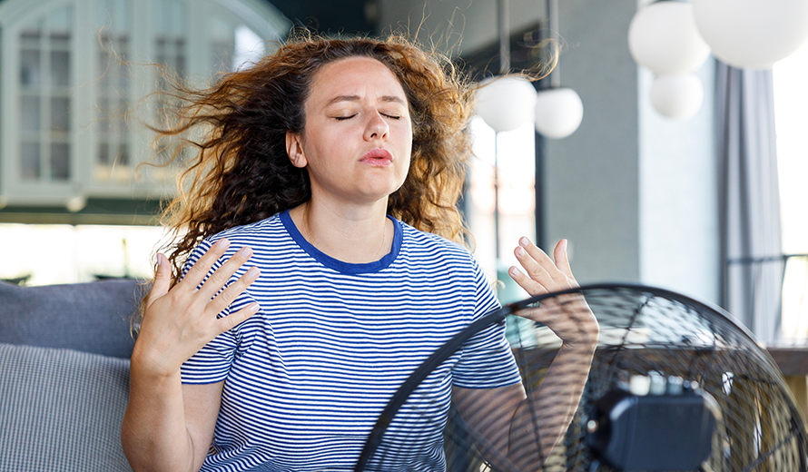 Verschwitzte Frau sitzt vor einem Ventilator.