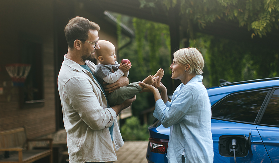 Vater, Mutter und Baby interagieren vor einem blauen Elektroauto.