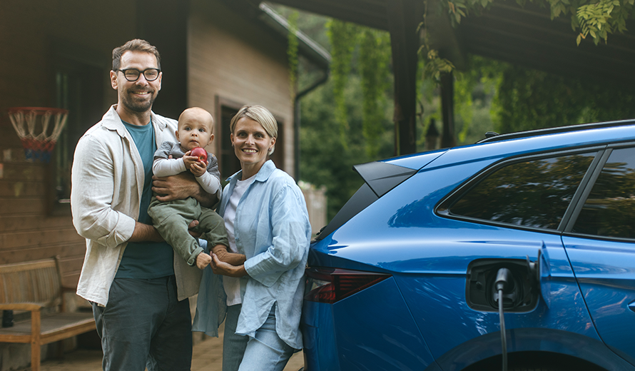 Vater, Mutter und Baby schauen in die Kamera, neben ihnen steht ein blaues Elektroauto.