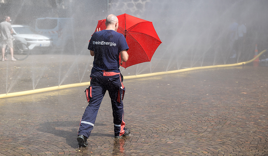 Ein Mann im RheinEnergie Blaumann geht mit rotem Regenschirm über den Rudolfplatz. 